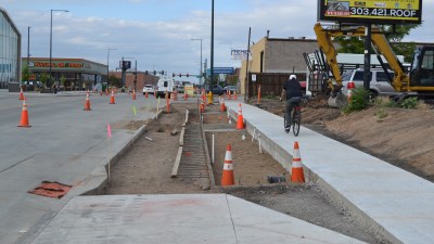 A man rides his bike on a brand new sidewalk, next to an unfinished  piece of the bikeway. Photo: David Sachs