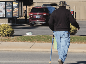 A man with a cane crosses in the middle of the street