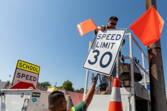 Department of Public Works employee Ernie Armijo hands a new speed limit sign to Danny Gonzales before it was installed on Evans Avenue Aug. 30. Photo: Andy Bosselman