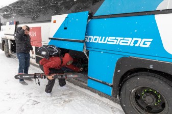 Person removes skis from cargo area of Snowstang bus