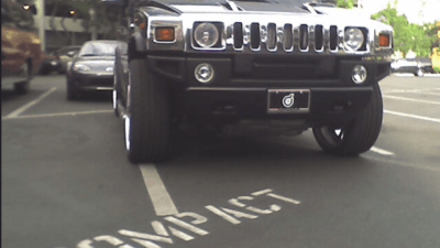 Photo Hummer parked over the lines in parking space labeled for compact vehicles