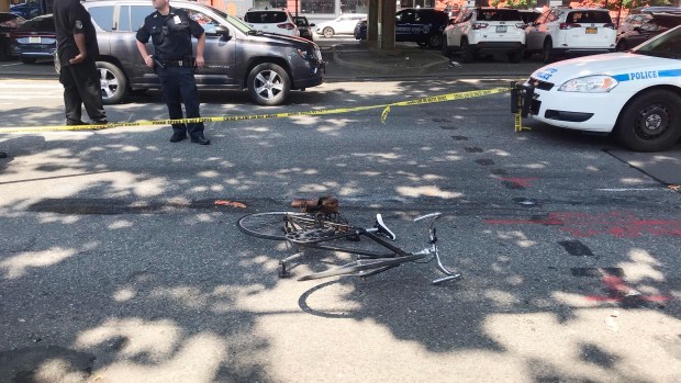Post-crash mangled bicycle on street with caution tape, police officer, and police car