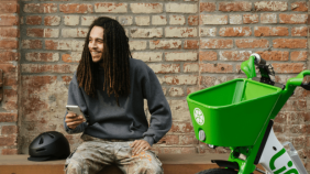 Man sits on a bench next to Lime bike and helmet