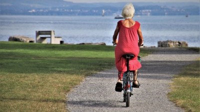 Person with grey hair wearing a dress rides a bike on a park trail